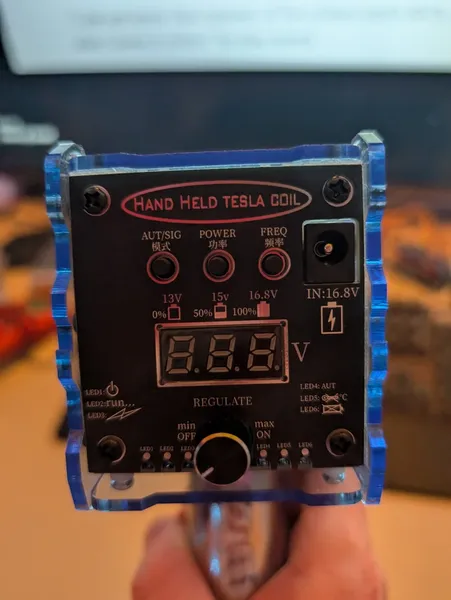 The handheld Tesla coil front panel showing AUT/SIG, POWER, FREQ buttons, REGULATE knob, and voltage display